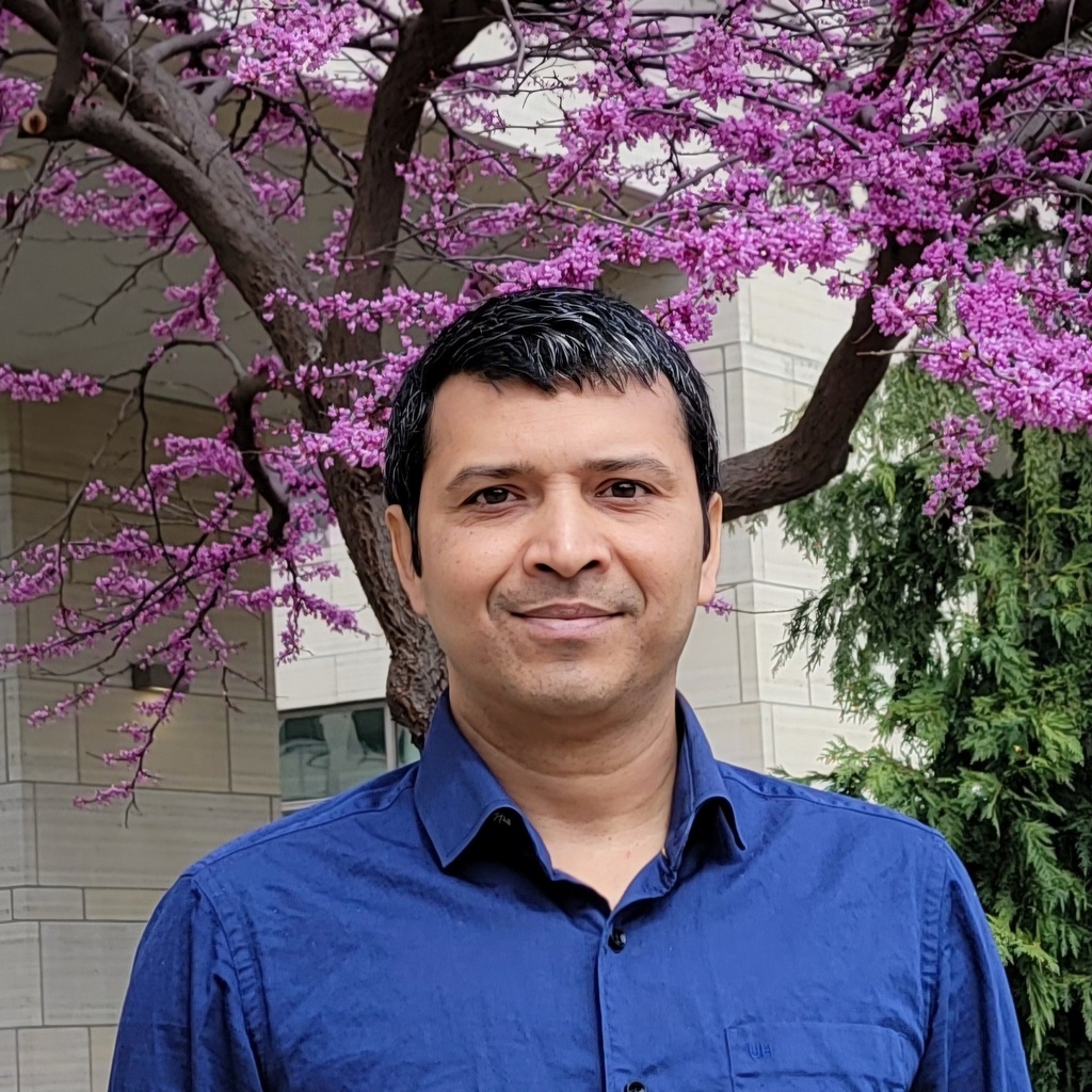 Photo of Prabhat standing outside in front of an eastern redbud tree in bloom