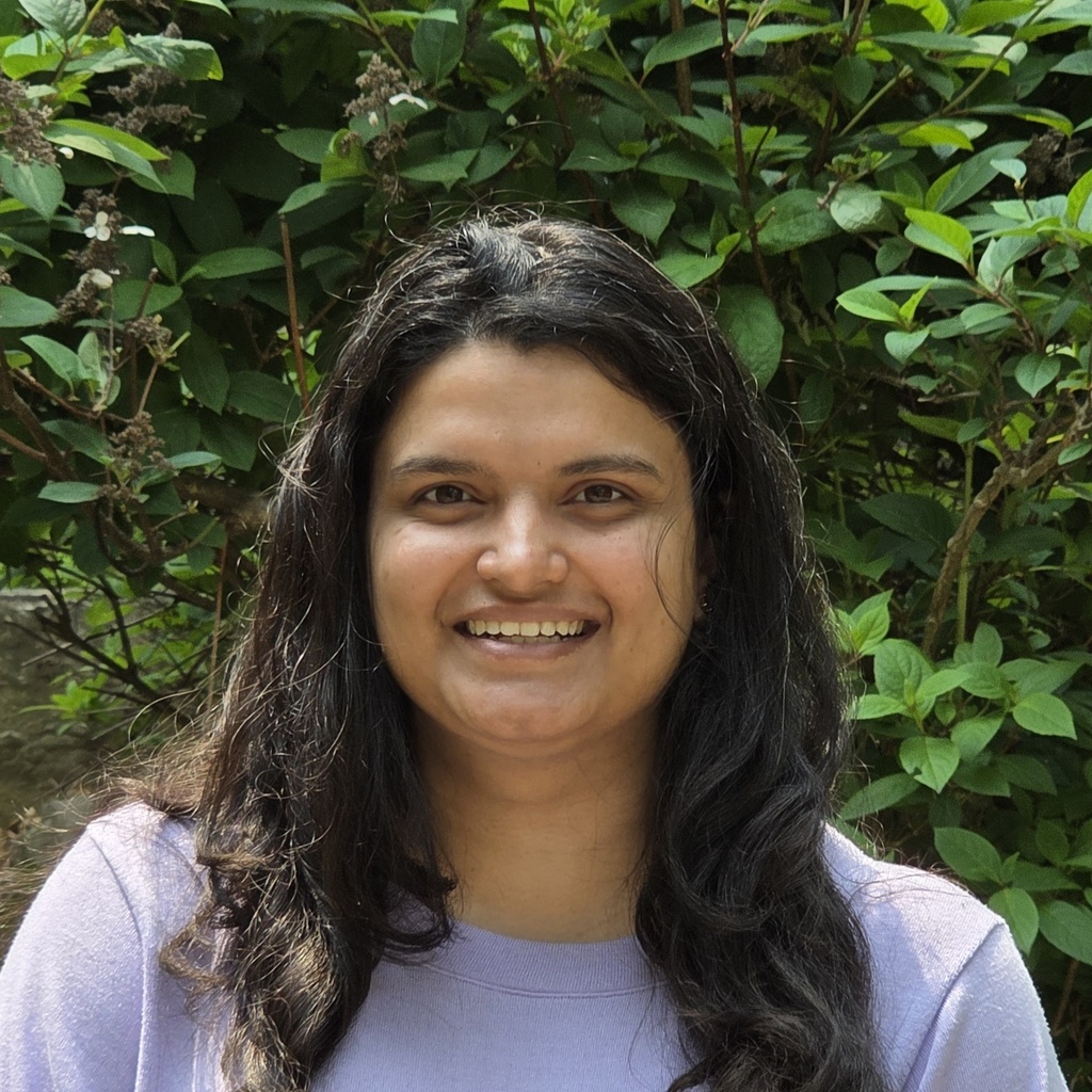 Head shot of Prerana standing outside in front of some green plants