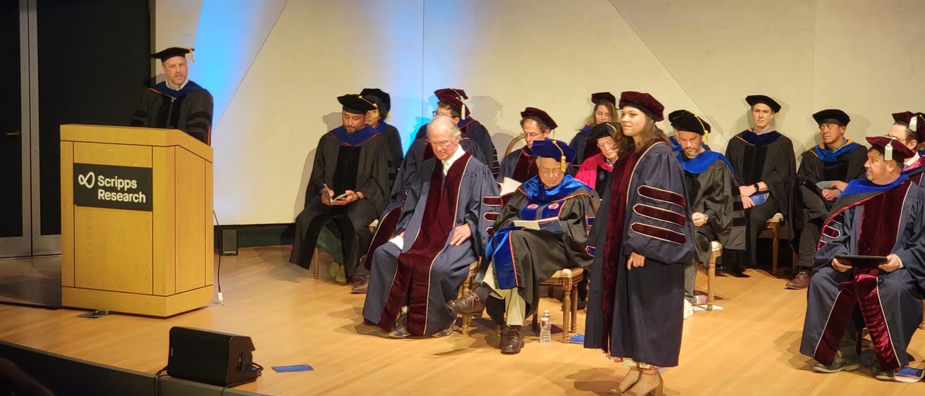 PhD graduates on stage with Seth introducing Val