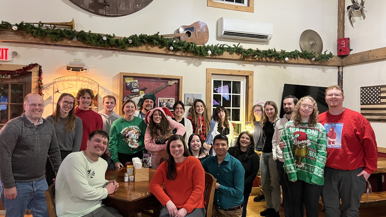 Lab members in holiday attire posing around a large wood table